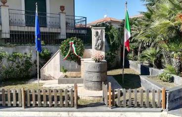 Il Monumento ai Caduti tra le bandiere italiana ed europea, con la corona d'alloro alla base